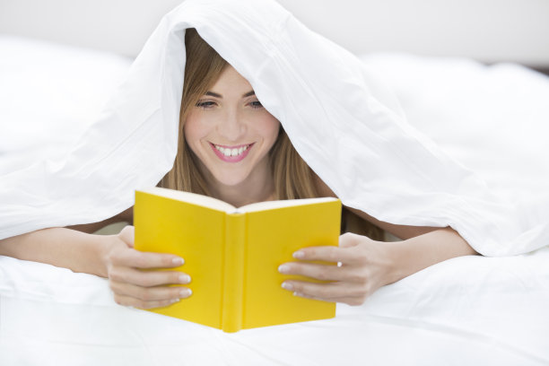 快乐的年轻女子在床上看书图片下载