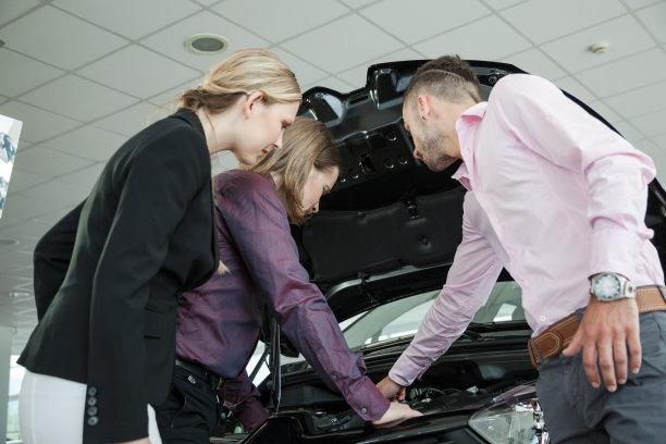 汽车销售员向幸福的年轻夫妇展示发动机的功能图片下载