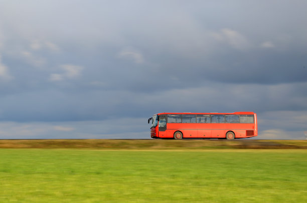 红色的公共汽车行驶在乡间小路上穿过田野图片下载