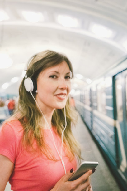 美丽女人在智能手机上听音乐，地铁背景图片下载