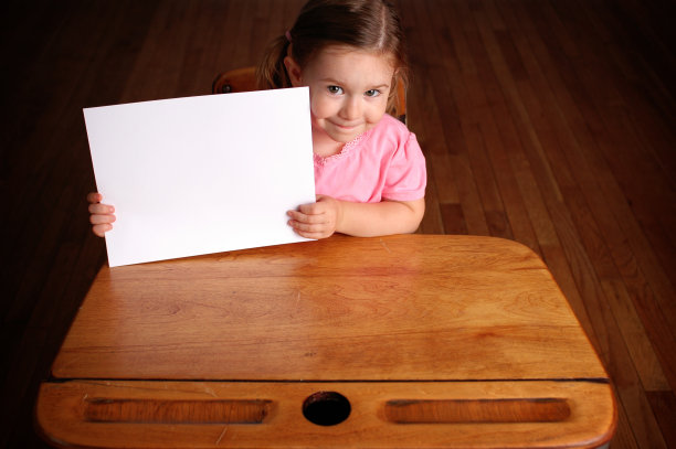 快乐的小女孩在课桌上拿着空白的牌子图片下载