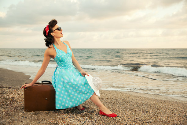 海滩上带着行李箱的年轻快乐女士图片下载