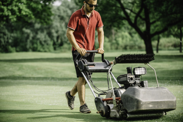 在高尔夫球场上移动果岭的草地管理员图片下载