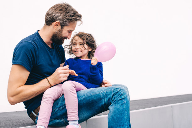 年轻的胡子父亲抱着小微笑的女儿与气球图片下载