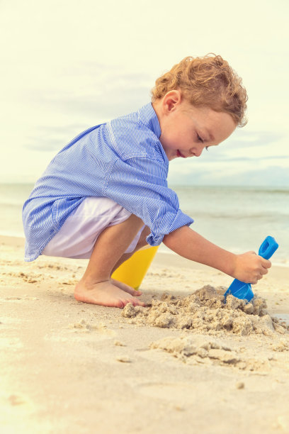 小男孩开始在海滩上建造沙堡图片下载