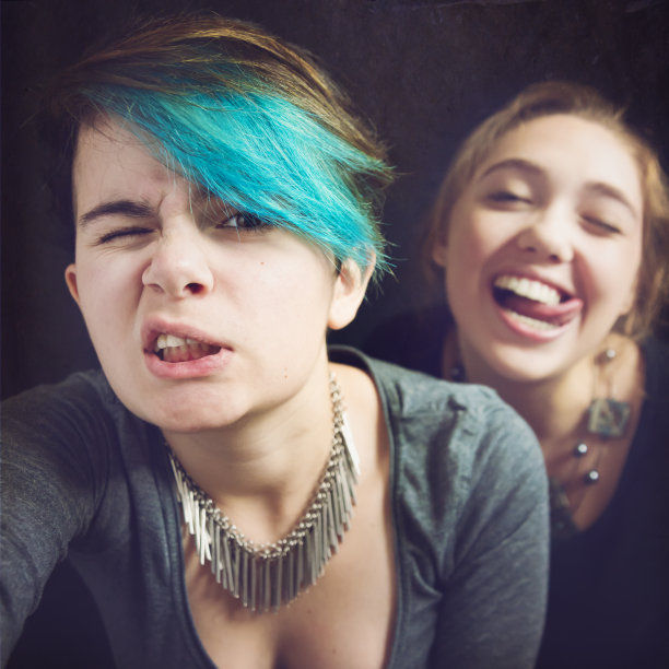 两个时尚的青少年在黑色背景上做鬼脸的自拍。图片下载