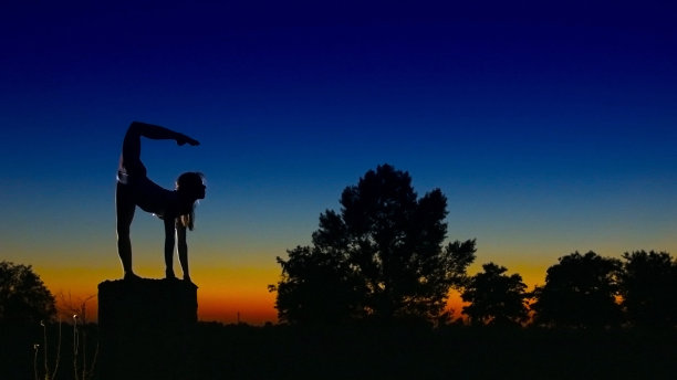 杂技女演员晚上在立柱上练习天蝎座的姿势图片下载