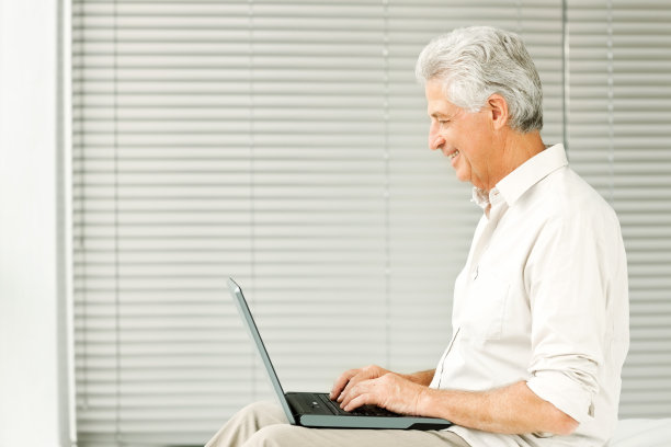 微笑的老人在卧室使用笔记本电脑图片下载