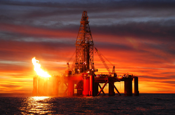 日落时海洋石油钻井平台的剪影。图片下载