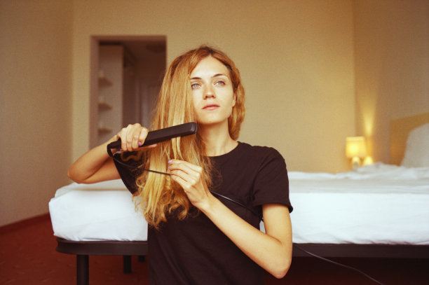 年轻女子用卷发器烫头发。图片下载