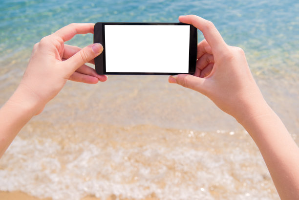 一个女人在海滩上用智能手机的照片图片下载