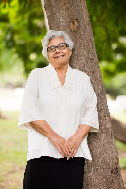 拉丁高级女子站在树旁微笑着图片下载