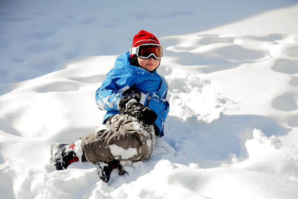 小男孩穿得严严实实地躺在雪地里图片下载