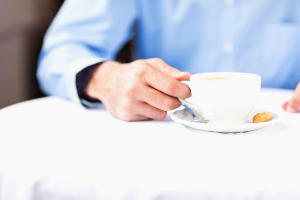 拿着咖啡杯和茶托坐在餐厅桌子旁的男人图片下载