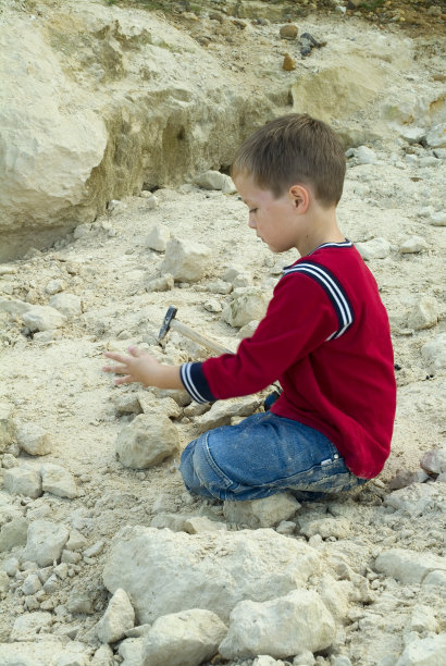 小男孩敲打着石灰石寻找化石图片下载