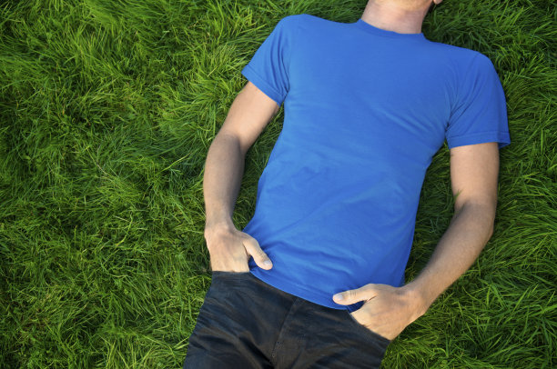 穿着蓝色t恤的男人躺在户外浓密的绿色草地上图片下载
