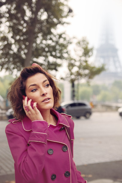 一个女人在街上拿着手机，朦胧的埃菲尔铁塔背景。图片下载