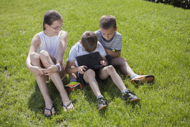 孩子们坐在草地上玩数字平板电脑图片下载