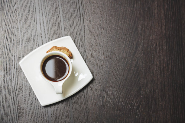 黑木桌上放着一杯咖啡和一块饼干。图片下载