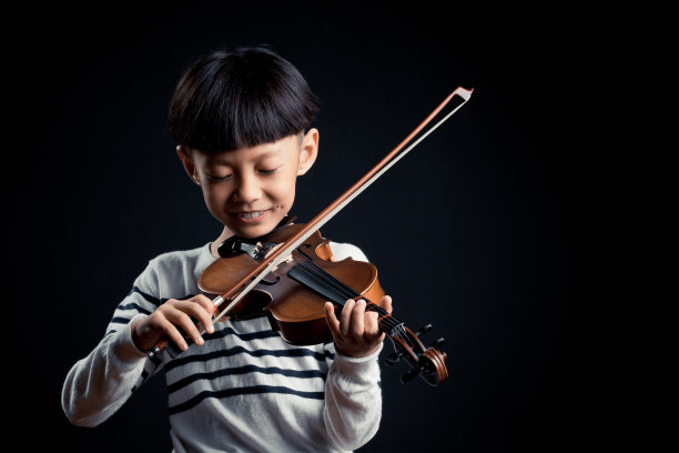 一个男孩在黑色的背景下独自拉着小提琴图片下载