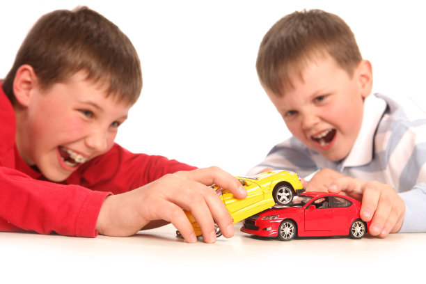 男孩情绪激动地笑着玩红色和黄色的玩具车。图片下载