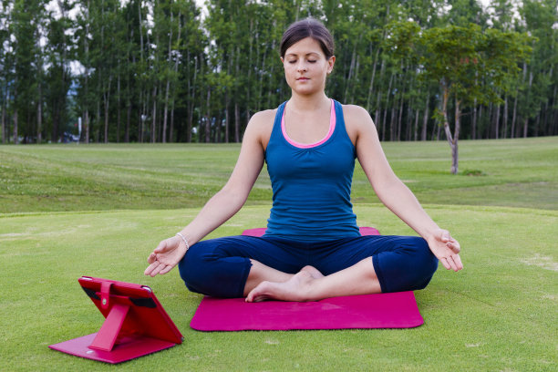 在平板电脑的帮助下，年轻女子在户外做瑜伽图片下载