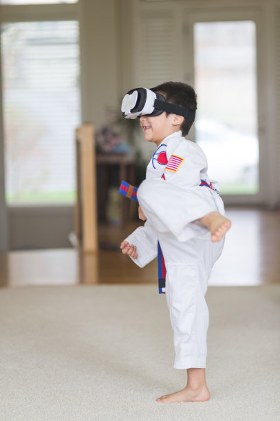 年轻的美国原住民穿着武术制服，戴着3D眼镜在客厅练习踢腿图片下载