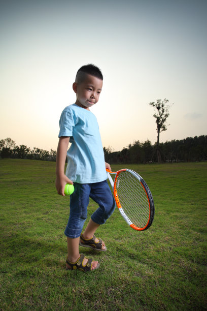 一个亚洲男孩在草坪上打网球图片下载