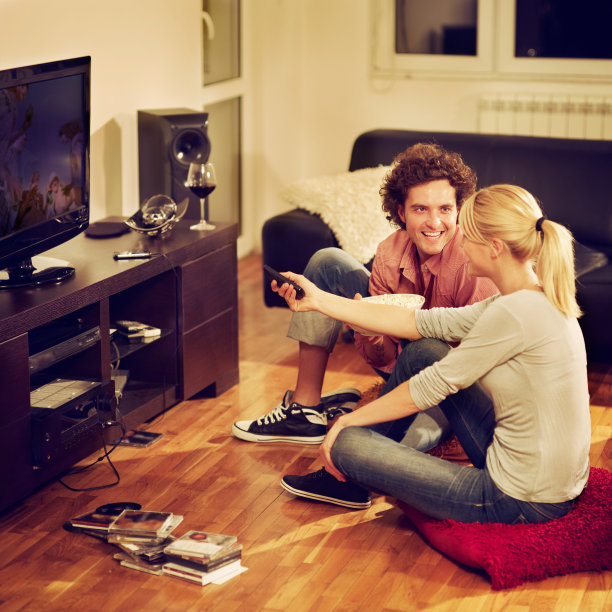 一对年轻夫妇坐在地板上看电视图片下载