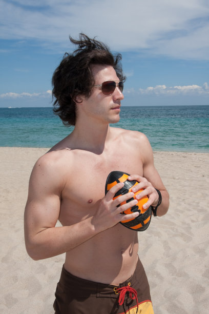 英俊的年轻人在沙滩上踢足球图片下载