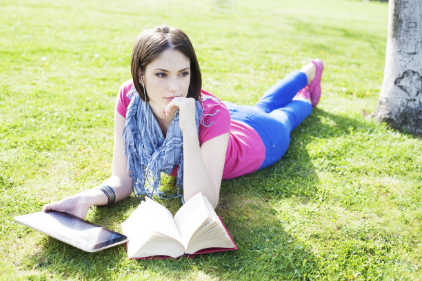 快乐的年轻女子躺在草地上，使用数码平板电脑图片下载