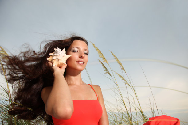 美丽的女孩把贝壳放在她的耳边图片下载