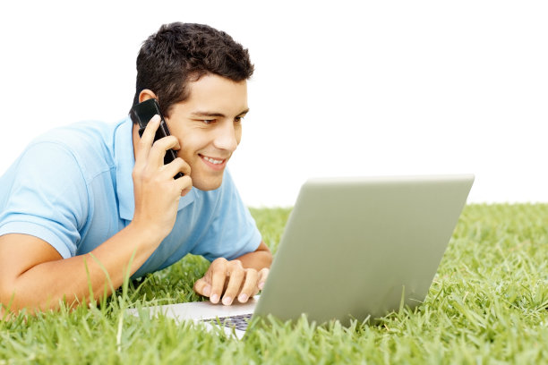 微笑的家伙躺在草地上用手机和笔记本电脑图片下载