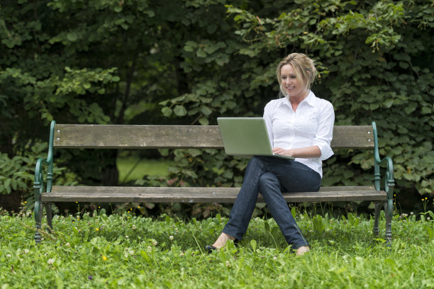 在公园的长椅上，微笑的年轻女子拿着笔记本电脑图片下载