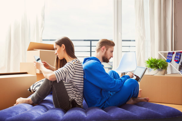 一对年轻夫妇坐在家里的床垫上，用着平板电脑图片下载