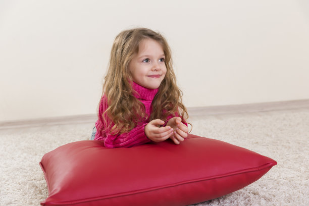 小女孩微笑着躺在红垫子上图片下载