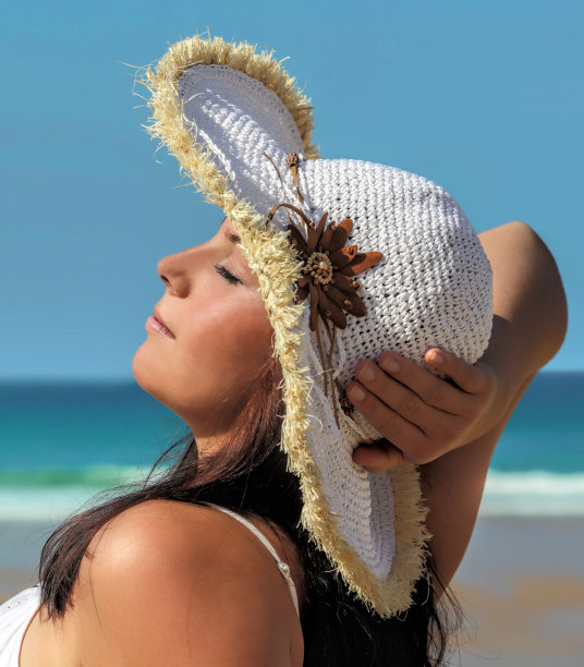 年轻的美女戴着太阳帽在海滩上晒太阳图片下载