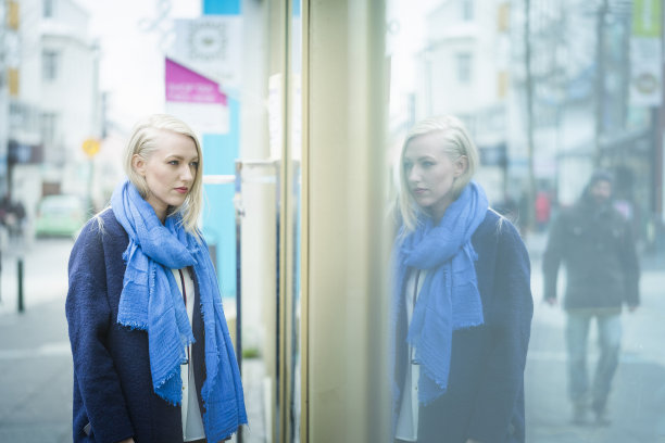 一个女人看着橱窗，玻璃上映出了她的影子图片下载