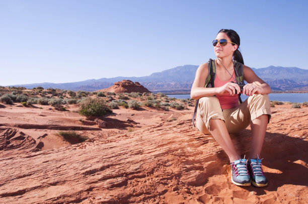 女徒步者在沙漠山丘上休息，背景是湖泊图片下载