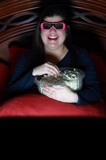 一个戴着3D眼镜看电视吃爆米花的女人图片下载