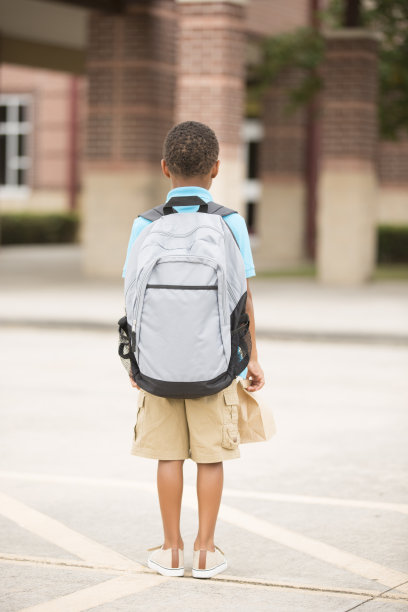 非洲裔，一个小男孩面对着教学楼。午餐,背包。图片下载