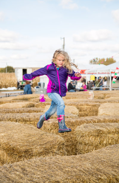 少女奔跑在秋季稻草捆迷宫的顶端图片下载