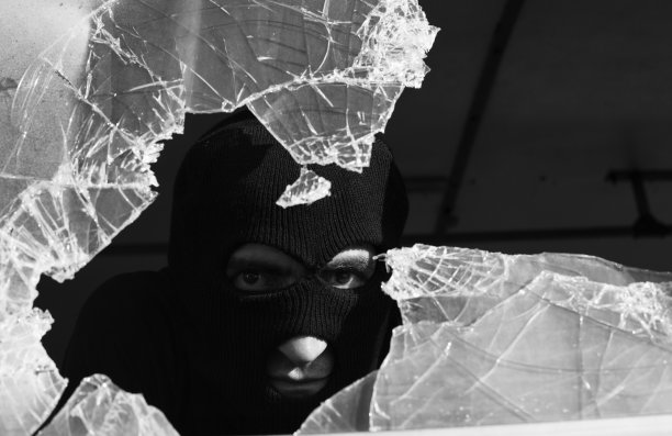 一个成年男子戴着面罩从碎玻璃后面偷窥图片下载