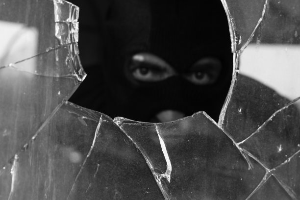 一个成年男子戴着面罩从碎玻璃后面偷窥图片下载