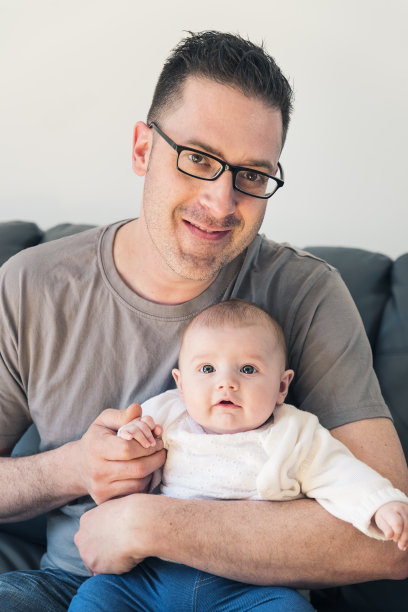 骄傲的父亲带着女儿坐在家里的沙发上。图片下载