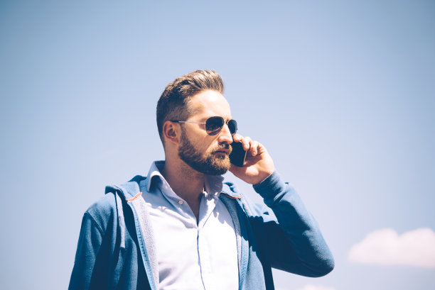 在蓝天下和手机聊天的大胡子男人图片下载
