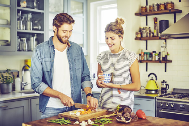 拿着咖啡杯的女人看着正在切胡萝卜的男人图片下载