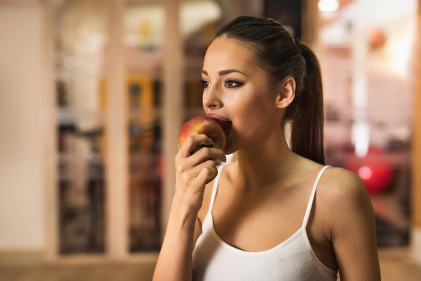 年轻女运动员在健身俱乐部咬苹果。图片下载