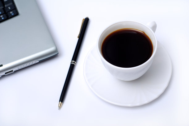 一杯咖啡和一支笔放在笔记本电脑旁边图片下载