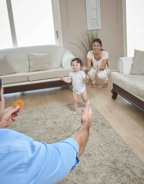 父母帮助婴儿在客厅地板上行走图片下载